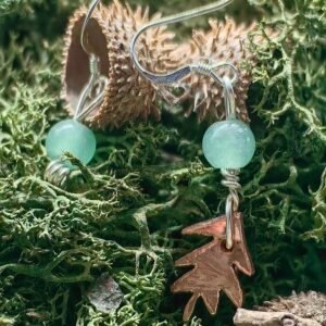 Boucle d'oreille artisanale en argent et cuivre éthiques, avec un petit pin gravé et une aventurine verte, faite main en France sur mousse végétale naturelle et coque de gland naturel.
