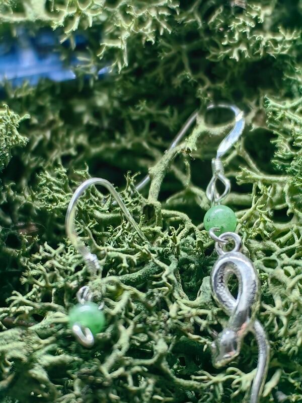 Gros plan sur le matériau des boucles d'oreilles Le Savoir du Serpent, montrant l'argent, le cuivre, et l'aventurine verte sur mousse végétale naturelle.