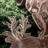 Gros plan sur le Blaireau sculpté du pendentif "taisson persévérant" perché sur un tronc couché entouré de fougères, fait main en France en argent et cuivre éthiques, hypoallergénique, sur de la mousse végétale naturelle.