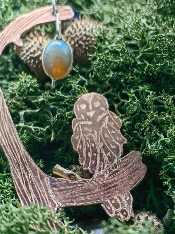 Gros plan de la Chouette chevêche sculptée sur le pendentif, "chevêche rêveuse" en argent et cuivre éthiques, hypoallergénique, fait main en France, symbole de sagesse sur de la mousse végétale naturelle.