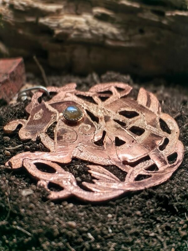 Pendentif "Cheval des mer" argent-cuivre et labradorite, collection Artéfacts chez Le Chêne Enchanté. Pendentif posé sur la terre de mon jardin comme un ancien trésor qu'un archéologue ou un historien aurait découvert après des siècles passés sous terre. Vu entière du pendentif.