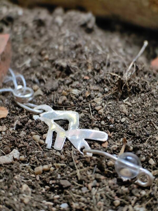 Pendentif bindrune "Energie" argent et cristal de roche déposé sur de la terre de mon jardin comme un trésor qu'un archéoloque ou historien trouverait après des siècles passés sous terre. Issu de la collection Artéfacts chez Le Chêne Enchanté. Vu du pendentif entier.