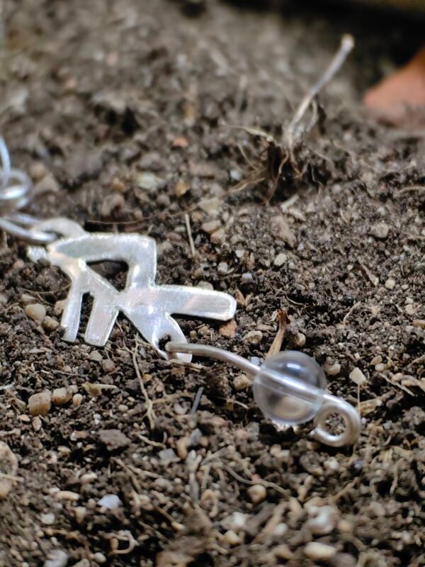 Pendentif bindrune "Energie" argent et cristal de roche déposé sur de la terre de mon jardin comme un trésor qu'un archéoloque ou historien trouverait après des siècles passés sous terre. Issu de la collection Artéfacts chez Le Chêne Enchanté. Vu du cristal de roche.