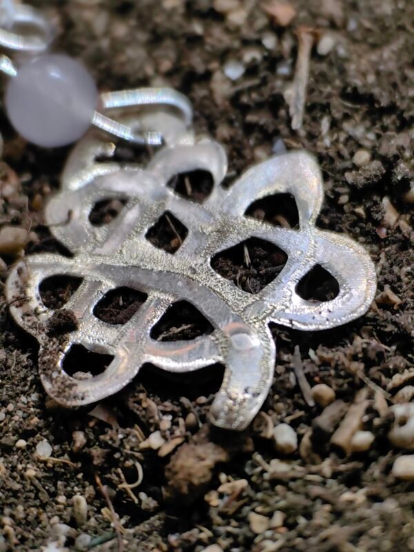 Pendentif "trèfle" celtique argent et quartz rose, posé sur de la terre de mon jardin comme un trésor qu'un archéologue ou historien aurait déterré après avoir passé des siècles sous terre. Collection Artéfacts chez Le Chêne Enchanté. Vu de près du trèfle celtique