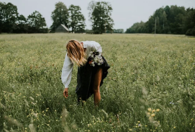 Jeune femme dans un champs de fleurs sauvages, cueillant ses fleurs pour les célébrations de Litha, article sur les plantes et fleurs de Litha chez Le Chêne Enchanté.