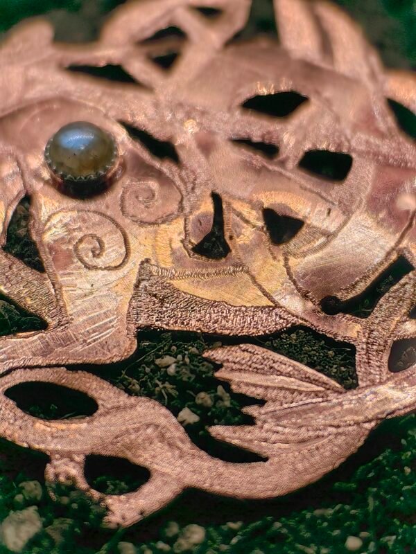 Pendentif "Cheval des mer" argent-cuivre et labradorite, collection Artéfacts chez Le Chêne Enchanté. Pendentif posé sur la terre de mon jardin comme un ancien trésor qu'un archéologue ou un historien aurait découvert après des siècles passés sous terre. Vu sur le bas du pendentif, sur la queue en forme de queue de poisson, les entrelacs, spirale et triqueta celtiques.