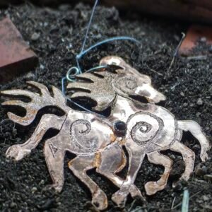 Pendentif "Sleipnir", le destrier d'Odin en argent-cuivre et tourmaline noire éthiques, de la collection Artéfacts chez Le Chêne Enchanté. Le pendentif est posé délicatement sur la terre de mon jardin comme si il avait été déterré par un historien ou archéologue après des siècles passé sous terre, tel un artéfact ancien. Sur son corps est gravé trois spirales motif celtique du mouvement. Pendentif d'inspiration celtique et nordique. Vu entière du pendentif