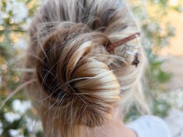 Pic à cheveux "lierre mystique" argent-cuivre et grenat. Collection Artéfacts chez Le Chêne Enchanté. Le pic à cheveux est déposé sur la terre comme l'aurait découvert un archéologue ou un histoirien après avoir passé des siècles enterrés. Le pic à cheveux se compose d'un long corps fin en cuivre qui passe entre les cheveux pour les maintenir ainsi qu'une feuille de lierre en argent maintenue par un fil d'argent. Pic à cheveux porté par un modèle féminin.