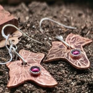 Boucles d'oreilles lierre mystique, en argent-cuivre éthiques et grenats éthiques, collection artéfacts chez Le Chêne Enchanté. Les boucles d'oreilles sont posées sur la terre de mon jardin comme l'aurait découvert un archéologue ou un historien après avoir passé des siècles enterré. Vu entière des boucles d'oreilles.