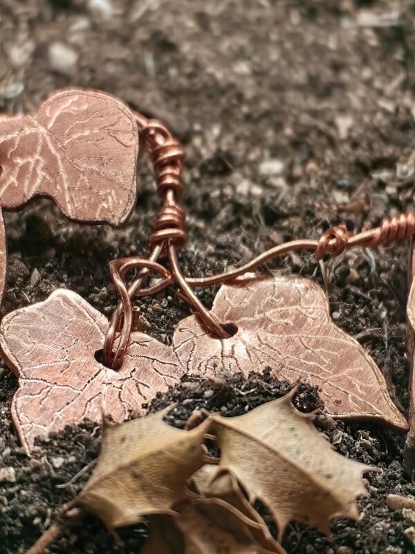 Vu entière du collier "lierre mystique" argent-cuivre éthiques et grenat, collection artéfacts chez Le Chêne Enchanté. Le collier est posé sur la terre de mon jardin, certaines de ses feuilles de lierres sont partiellement enterrées comme l'aurait découvert un archéologue ou un histoirien après que le collier ait passé des siècles sous terre.