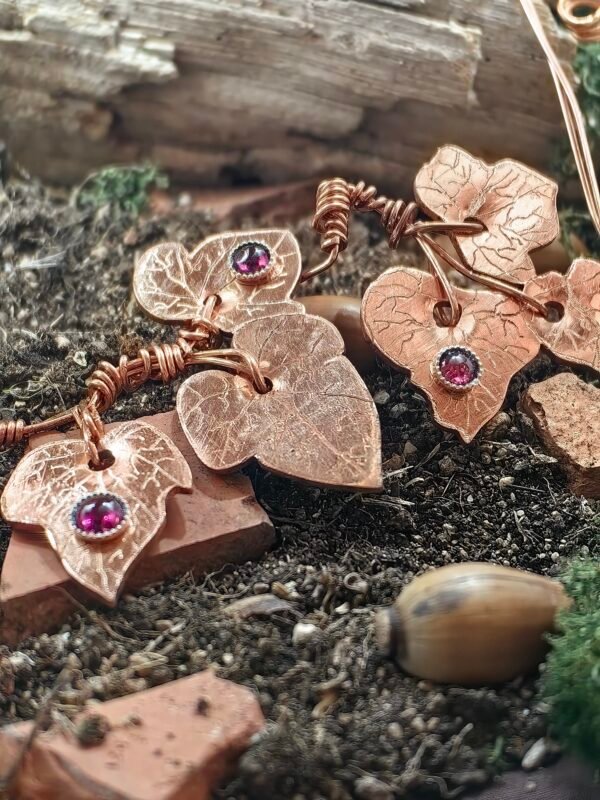 Vu de la partie droite du collier "lierre mystique" argent-cuivre éthiques et grenat, collection artéfacts chez Le Chêne Enchanté. Le collier est posé sur la terre de mon jardin, certaines de ses feuilles de lierres sont partiellement enterrées comme l'aurait découvert un archéologue ou un histoirien après que le collier ait passé des siècles sous terre.