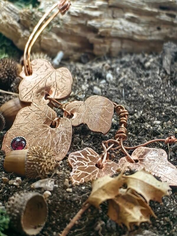 Vu de la partie gauche du collier "lierre mystique" argent-cuivre éthiques et grenat, collection artéfacts chez Le Chêne Enchanté. Le collier est posé sur la terre de mon jardin, certaines de ses feuilles de lierres sont partiellement enterrées comme l'aurait découvert un archéologue ou un histoirien après que le collier ait passé des siècles sous terre.