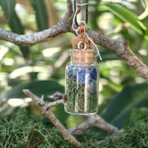 Pendentif fiole Talisman des Fées, lapis-lazuli, mousse végétale naturelle, cuivre, verre et liège, collection Artéfacts chez Le Chêne Enchanté. Le pendentif est suspendu à une branche de chêne entouré de mousse végétale naturelle dans la lumière du petit matin. Le pendentif est présenté porté par la branche. Ce pendentif est un cadeau du Petit Peuple, il protège, ancre et veille sur son porteur. Vu éloignée du pendentif. Tous les bijoux et photographies sont la propriété exclusive de : Le Chêne Enchanté. Toute reproduction est formellement interdite.