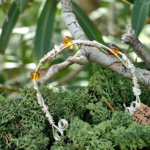 Bracelet Lueur d'hiver en argent tressé et ambres de la collection Artéfacts chez Le Chêne Enchanté suspendu à une branche de chêne et de mousse végétale naturelle verte. Vu entière du bracelet. Ce bracelet évoque la lumière même lorsque tout est gris, une lueur au coeur de l'hiver, l'équilibre de l'argent métal lunaire et l'ambre, pierre solaire. Tous les bijoux et photographies appartiennent à Le Chêne Enchanté et sont interdits de reproduction.