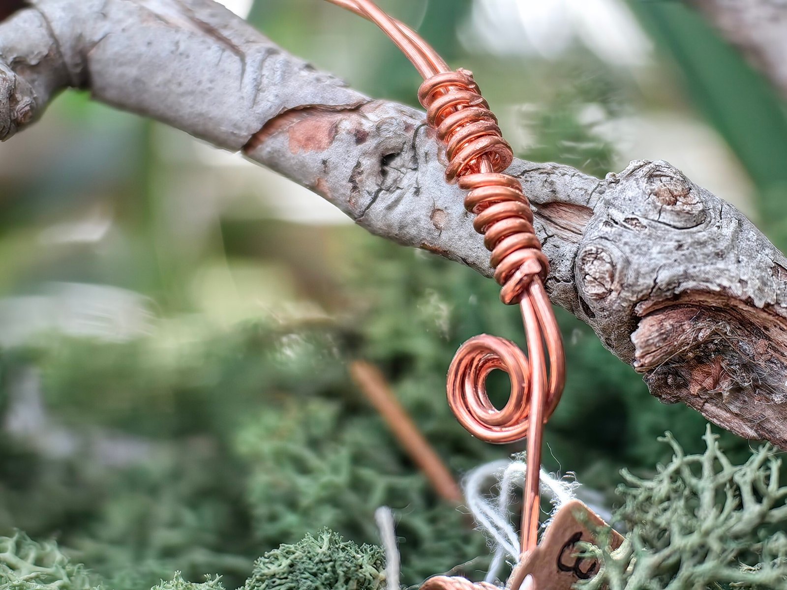 Bracelet Force intérieure en fils de cuivre tressés et grenat en perle, collection Artéfacts chez Le Chêne Enchanté. Le bracelet incarne les forces telluriques, l'amour et la protection. Ce bracelet réglable sous forme de jonc souple repose sur une branche de chêne au milieu d'une mousse forestière verte naturelle. Le bracelet se termine par deux spirales à chaque de ses extrêmités. Vu de près du tressage et de deux spirales fermant le bracelet. Tous les bijoux et photographies sont l'oeuvre de : Le Chêne Enchanté et interdite de reproduction.