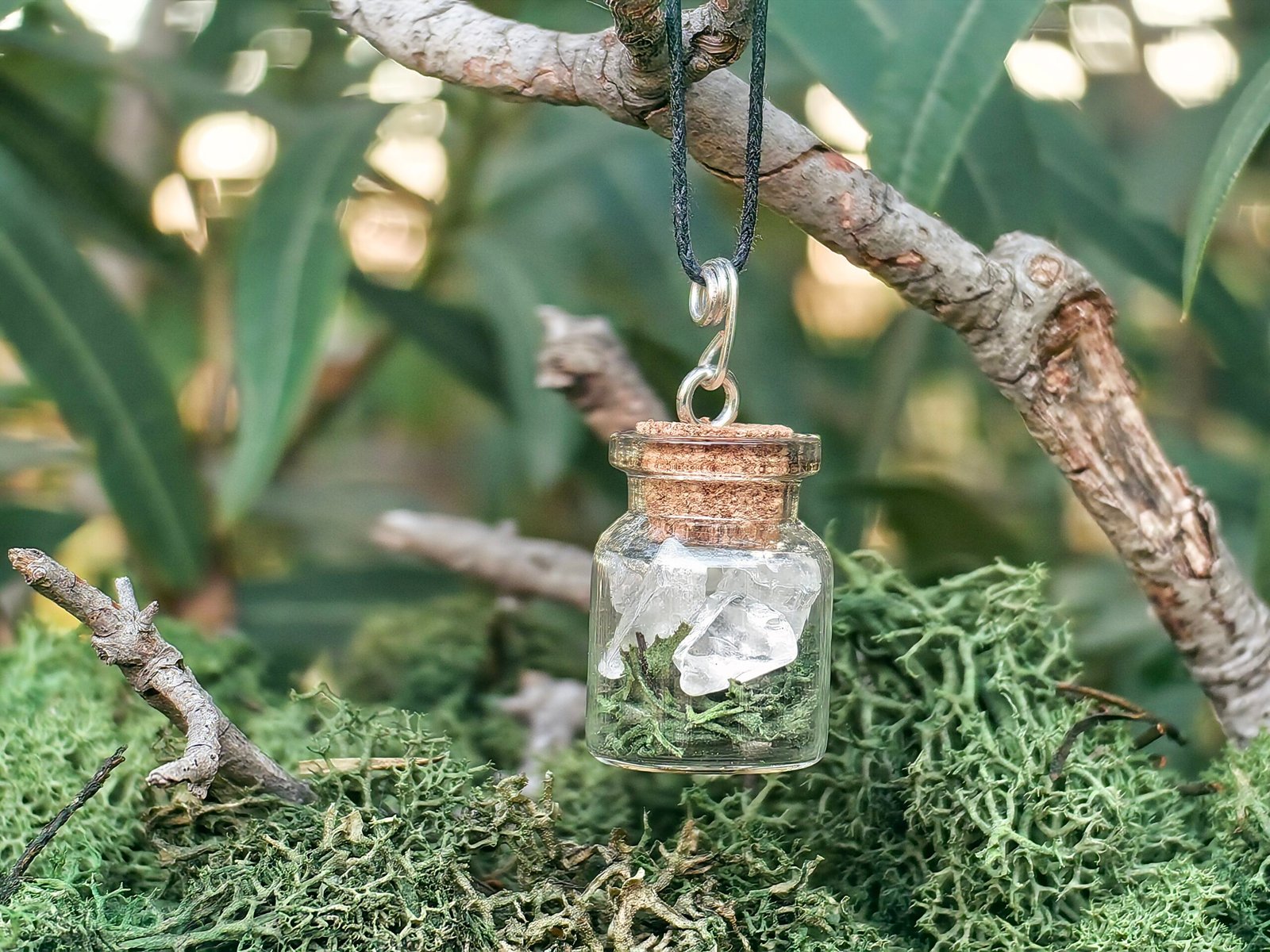Pendentif fiole Potion des fées, argent, cristal de roche, mousses naturelle végétale, verre et bouchon de liège de chêne, collection Artéfacts chez Le Chêne Enchanté. Le pendentif repose sur une branche de chêne entourée de mousse naturelle végétale de la forêt. Le pendentif fiole Potion des fées apporte clarté, ancrage, vision et mémoire de la Terre. Vu entière du pendentif. Tous les bijoux et photographies appartiennent exclusivement à : Le Chêne Enchanté. Toute reproduction est strictement interdite.